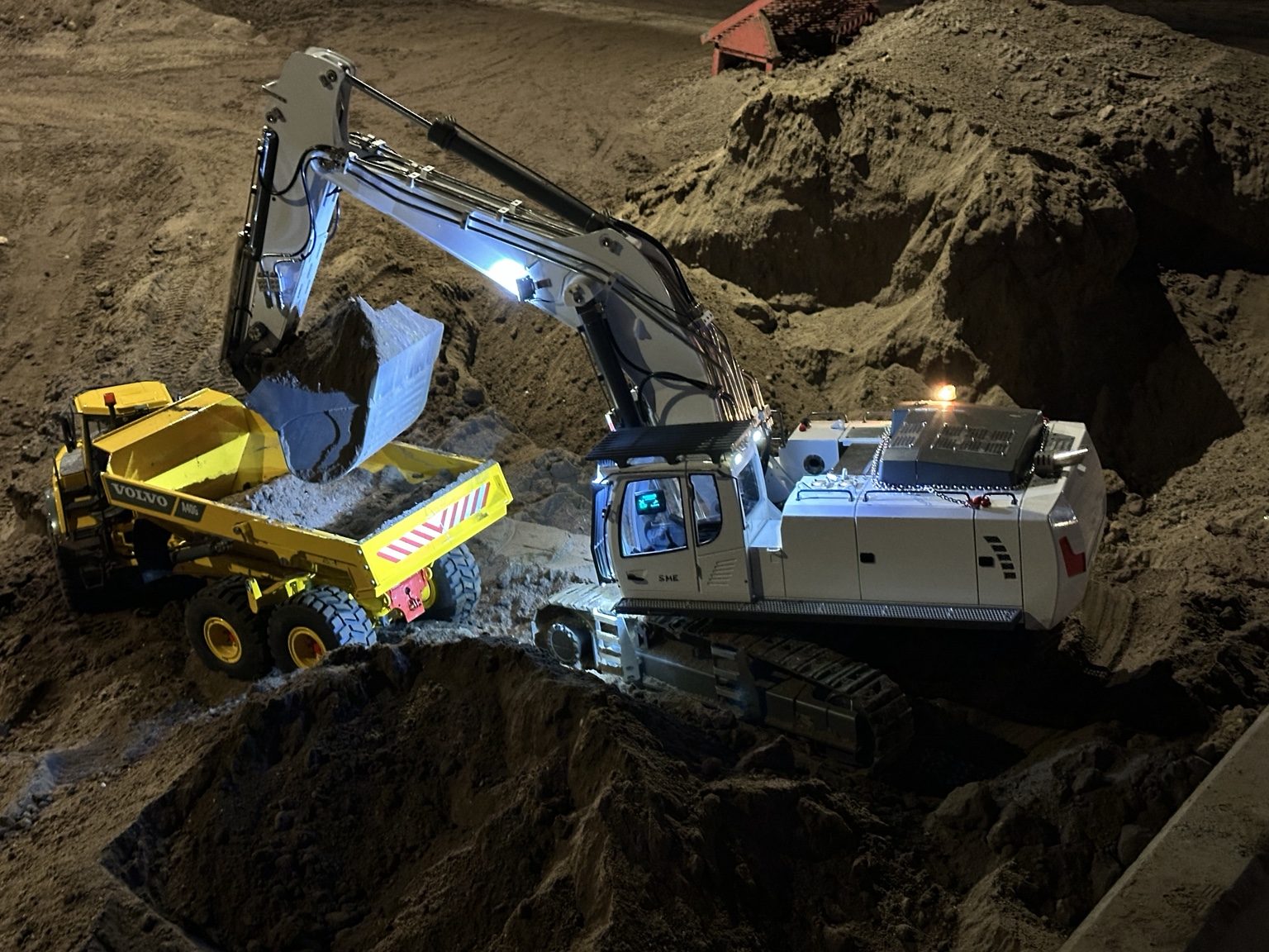 Raupenbagger belädt Volvo Dumper bei Nacht